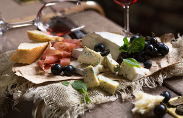 Assorted cheeses on wooden board. Camembert, cheese with blue mildew, gouda, hard cheese, strawberries, mint leaves, knives for cheese.