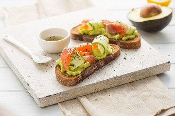 sandwich with avocado and salmon on a light background, green onions and gluten-free grain bread, radishes and cucumbers. concept diet food, copy space, sandwich take away, healthy fast food