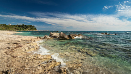Big rocks and rocky coastline with clear green sea under a blue sky and white clouds at the west-coast of Central Greece