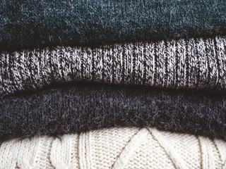 Pile of chunky winter sweaters laying on dark textured desk or table.