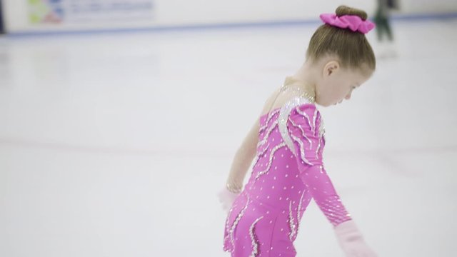 Little figure skater in pink dress practicing on the indoor ice rink.