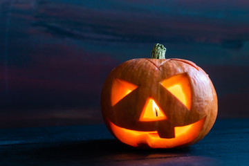 the orange glow from the burning candle inside the pumpkin in witch hat on a wooden table and Halloween with a black background
