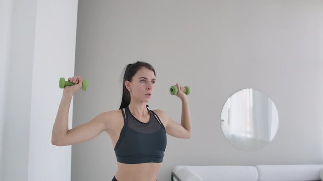 Raise the dumbbells over your head performing exercises for the shoulders. Training at home in the apartment