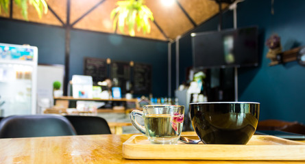 Black coffee mugs and tea mugs rest on a wooden tray placed on a wooden table in a coffee shop.