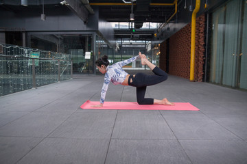 Young attractive smiling woman practicing yoga, sitting in One Legged King Pigeon exercise, Eka Pada Rajakapotasana pose, working out, wearing sportswear, grey pants, bra, indoor full length, home