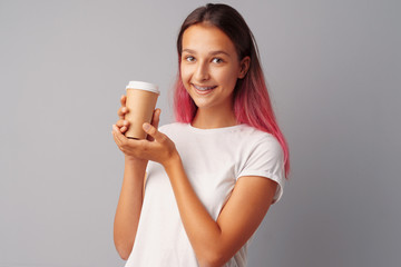 Nice teenager girl holding a cup of coffee over a gray background.