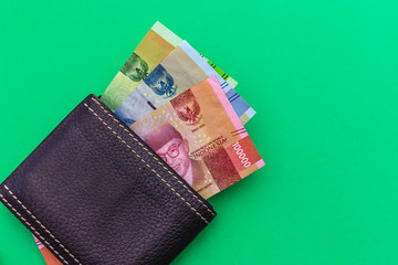 Black leather Men's Wallet with Indonesia rupiah cash on green background. Place for text.