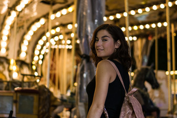 Young woman in a fair, carousel lights in the background