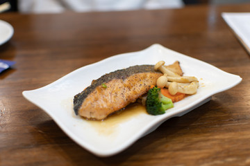 Salmon steak with vegetables on a white plate on a wooden table.