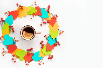 Autumn composition mug with hot tea and lemon. Paper colored leaves branches berries on white background The concept of autumn. flat lay top view