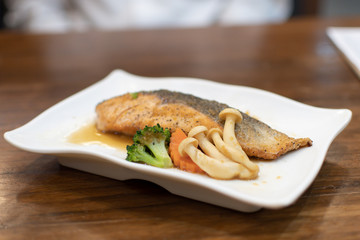 Salmon steak with vegetables on a white plate on a wooden table.