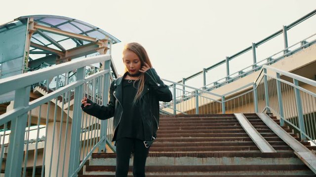 Teenager girl in black leather jacket walking down stairs on urban background. Rock girl in leather jacket going down on staircase bottom view