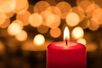 Red wax candle burning in front of bokeh background