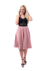 Carefree happy blonde young woman smiling while walking and talking on the cell phone. Full body isolated on white background. 