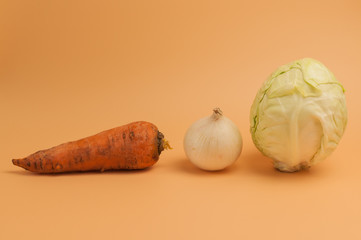 organic carrots,onions and cabbage on beige background,unpeeled sweet carrots,onions and cabbage for soup, minimalist style vegetables from the garden,vitamins,vegetarian food,healthy eating concept.