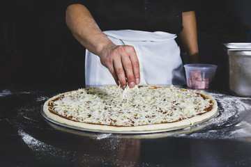 Chefs hand putting cheese on the pizza in black background.