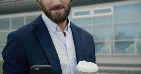 Closeup of young handsome office Manager texting Messages and drinking Coffe. Portrait of attractive bearded Man with brunette curly hair using Smartphone. People. Social Network. Apps. Technology. - Powered by Adobe