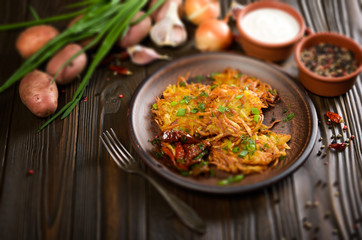 Homemade tasty potato pancakes in clay dish with sun-dried tomatoes and sour cream