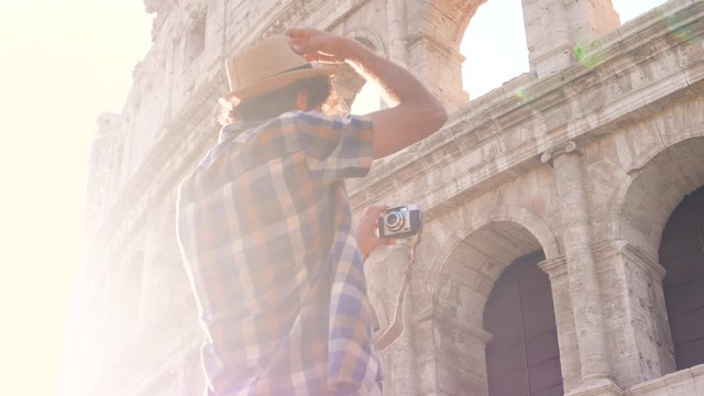 Happy young man tourist with bike wearing shirt tanding on a column taking funny pictures and selfies at colosseum in Rome, Italy at sunrise.