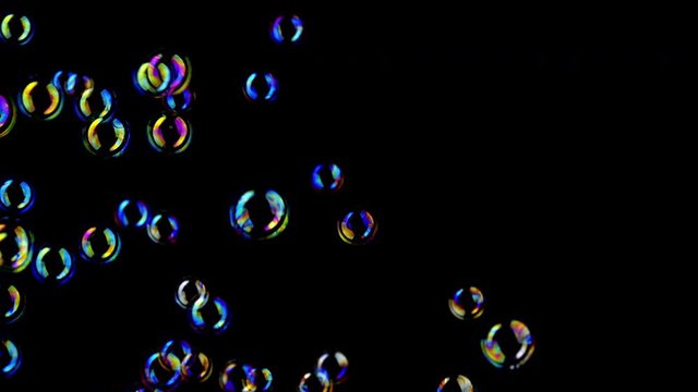 Colorful soap bubbles fly across black background. 