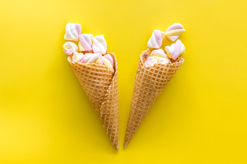 Sweet desserts. Marshmallows in ice cream waffle cone on yellow background top view