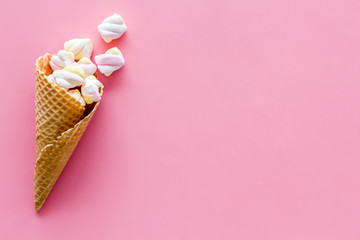 Sweet desserts. Marshmallows in ice cream waffle cone on pink background top view copy space