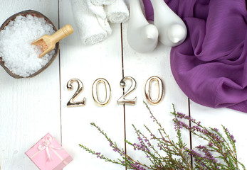 SPA set and gold numbers 2020 on a white wooden board with a purple cloth, figures of birds and a sprig of heather.