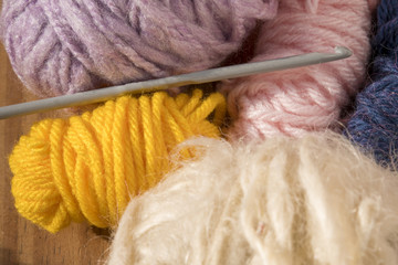 Ovillos de lana de colores varios y aguja de tejer crochet. Amarillo, lila, rosa y blanco.