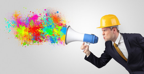 Fototapeta premium Young architect constructor yelling with megaphone with and colorful splash concept