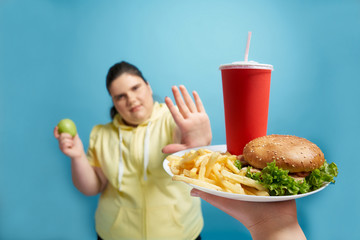 Young fat girl refusing to eat fastfood on white plate