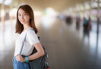 An  Asian woman is carrying a backpack, smiling and looking at the side