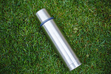 Thermos of stainless water, isolated on grass background.