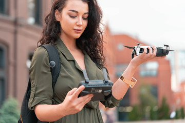 Young beautiful woman launching drone quadcopter at urban background. cityscape. modern device.