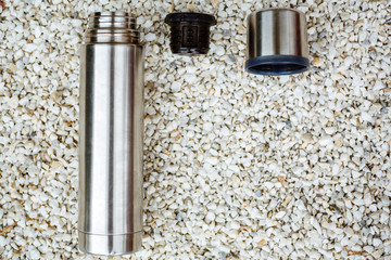 Stainless steel thermos for hot drinks, isolated on white stones.