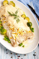 Baked white fish fillet in a thick sauce with vegetable side dish.
