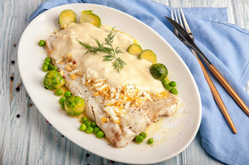 Baked white fish fillet in a thick sauce with vegetable side dish.