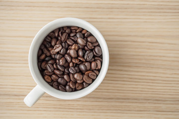 fresh roasted coffee beans in white cup on wood table, top view