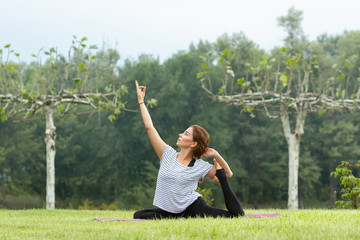 Young beautiful woman doing yoga exercise in green park near the pond. Exercices for improve the flexibility. Wellbeing and wellness. Healthy lifestyle and fitness concept.