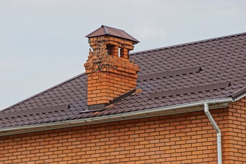 destroyed chimney pipe made of brown brick on the tiled roof of the house