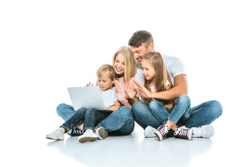 positive parents looking at laptop and waving hands with kids on white