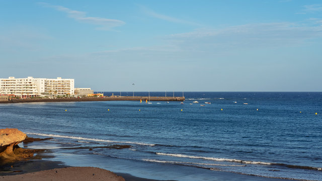 Afternoon views of the empty volcanic beach towards the resort hotels, restaurants and the small bay in the bohemian village of El Medano in Granadilla de Abona, Tenerife, Canary Islands, Spain