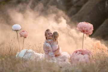 A little girl hugs mom sitting in a field surrounded by unreal big pink decorative flowers
