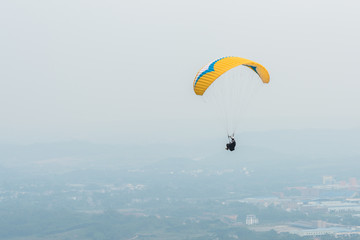 Aerial photography of a yellow paraglider flying over the town in the smoggy weather