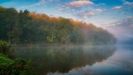 Fall colour reflected in the still waters of foggy morning Lake in Hungary