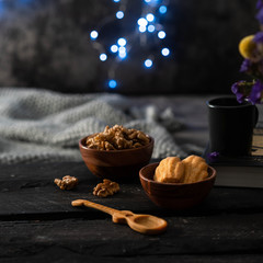 Fototapeta premium Madeline cookies, in a wooden bowl, walnuts in a bowl, dark Woden backdrop, festive lights background, cozy living room interior