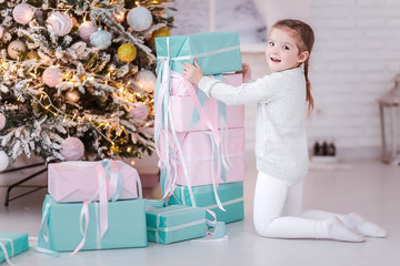Happy little girl builds a pyramid of gifts near the New Year tree