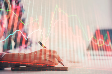 A woman hands writing information about stock market in notepad. Forex chart holograms in front....