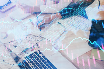 A woman hands writing information about stock market in notepad. Forex chart holograms in front. Concept of research. Double exposure