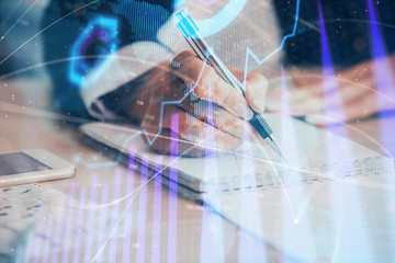 A woman hands writing information about stock market in notepad. Forex chart holograms in front. Concept of research. Multi exposure