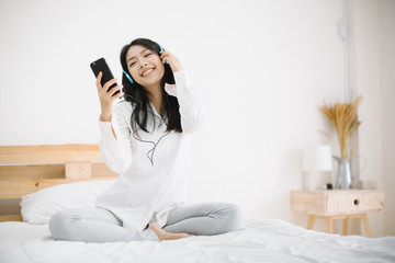 young woman relaxing and listening to music using headphones, she sitting in bed